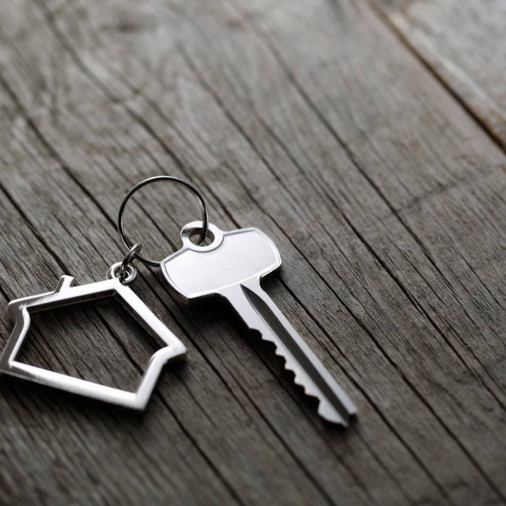 House key with a house-shaped keychain on a dark wood table